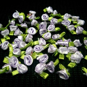 Könnte beinhalten: Eine große Menge kleiner, lavendelfarbener Satinbandblumen mit grünen Stielen. Die Blumen sind in einem zufälligen Muster auf einem schwarzen Hintergrund angeordnet.