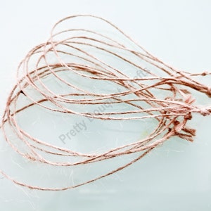 May include: A bundle of natural twine, made from jute, in a light brown color. The twine is in a loose pile, with some strands knotted together.