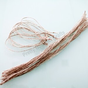 May include: A bundle of natural twine, some of which is tied into loops. The twine is a light brown colour and is lying on a light blue surface.