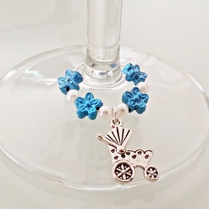 Könnte beinhalten: Blauer und weißer Glasanhänger mit einem silbernen Kinderwagen-Anhänger. Der Anhänger besteht aus Perlen und Blumen und ist dazu bestimmt, als Weinglasanhänger verwendet zu werden.