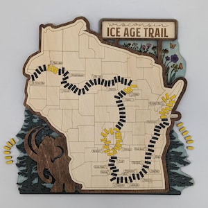 May include: Wooden map of Wisconsin with the Ice Age Trail highlighted. The map is light-colored with a dark brown border and features a route marked with black and yellow segments. The text "Wisconsin Ice Age Trail" is at the top.