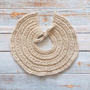 May include: A beige knitted collar with a rounded shape and a tied opening in the back.