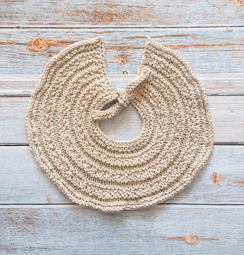May include: A beige knitted collar with a rounded shape and a tied opening in the back.