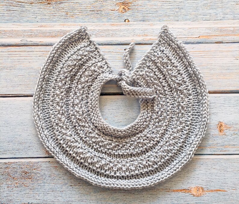 May include: A gray knitted collar with a tie closure. The collar is made of a soft, textured yarn and has a simple, elegant design.