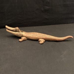 May include: A gold-toned metal alligator nutcracker. The alligator is depicted with an open mouth, showing its teeth, and a textured body.
