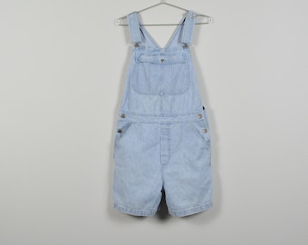 Puede incluir: Pantalón vaquero de mezclilla azul claro con piernas cortas y tirantes ajustables. El mono tiene un solo bolsillo delantero y múltiples cierres de botón.