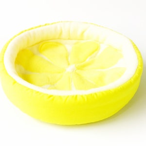 Peut inclure: Un lit pour animal de compagnie en forme de citron jaune avec une doublure en peluche blanche. Le lit est conçu pour ressembler à une tranche de citron.