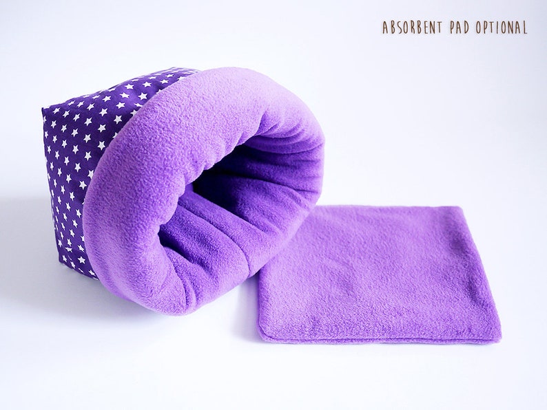 May include: Purple and white star patterned pet bed with a purple fleece lining.  The bed is shaped like a burrow and has a separate purple fleece pad.  Absorbent pad optional.