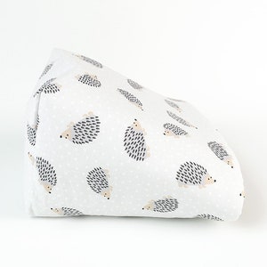 May include: A white fabric wedge pillow with a pattern of gray and beige hedgehogs on a white background with small white dots.