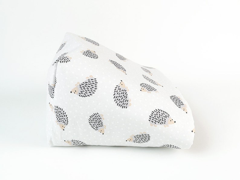 May include: A white fabric wedge pillow with a pattern of gray and beige hedgehogs on a white background with small white dots.