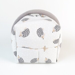 May include: A gray and white hedgehog-patterned fabric pet bed with a gray fleece lining. The bed is shaped like a house with a rounded top.