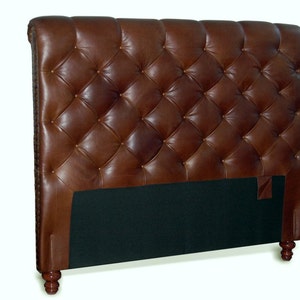 May include: A brown leather headboard with a tufted design and wooden legs. The headboard is upholstered in a rich brown leather and features a diamond-shaped tufting pattern. The headboard is supported by four wooden legs.