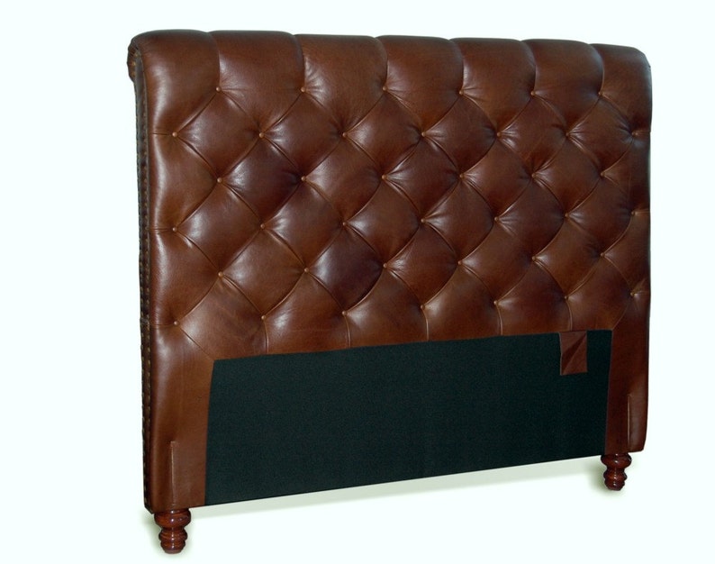 May include: A brown leather headboard with a tufted design and wooden legs. The headboard is upholstered in a rich brown leather and features a diamond-shaped tufting pattern. The headboard is supported by four wooden legs.