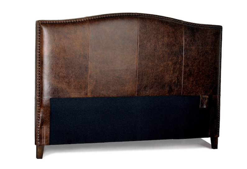 May include: A brown leather headboard with a curved top. The headboard has a dark brown finish with visible grain and is accented with small, evenly spaced studs along the edges. The lower section is covered in a dark blue fabric.