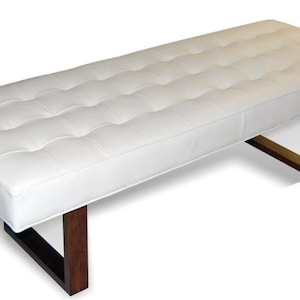 May include: A white tufted bench with a wooden frame and metal legs. The bench has a rectangular shape and a simple design.