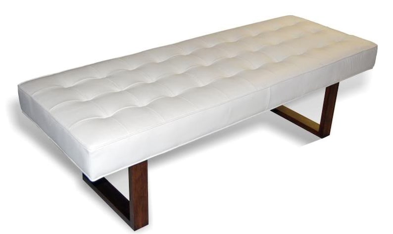 May include: A white tufted bench with a wooden frame and metal legs. The bench has a rectangular shape and a simple design.