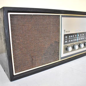 May include: A vintage Emerson AM/FM radio with a woodgrain cabinet and a black speaker grille. The radio has a silver face with a blue tuning dial and silver knobs.