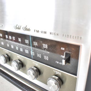 May include: A vintage silver and black AM/FM radio with a silver faceplate and black knobs. The radio has a dial with numbers from 54 to 160 and the text "Solid State FM-AM HIGH FIDELITY".