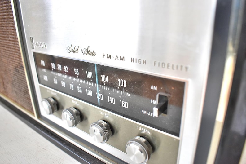 May include: A vintage silver and black AM/FM radio with a silver faceplate and black knobs. The radio has a dial with numbers from 54 to 160 and the text "Solid State FM-AM HIGH FIDELITY".