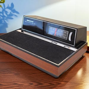 May include: Vintage Admiral Solid State FM-AM radio with a black top and wood-grain base. The radio features a tuning dial with a red indicator and a silver trim. The radio is on a wooden surface.