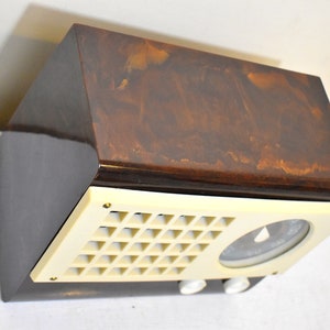May include: A vintage brown and cream colored radio with a dial and a speaker grille. The radio has a wood veneer finish.