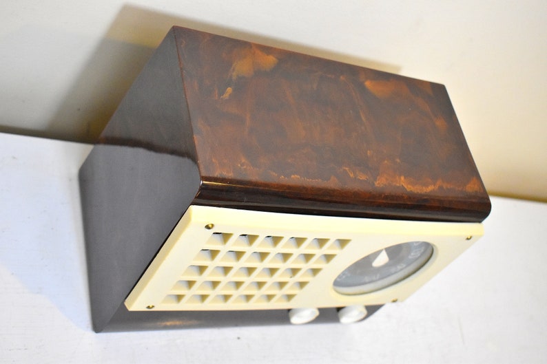 May include: A vintage brown and cream colored radio with a dial and a speaker grille. The radio has a wood veneer finish.
