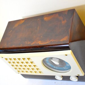 May include: A vintage brown and cream radio with a dial and three knobs. The radio has a marbled brown finish and a cream-colored front panel.