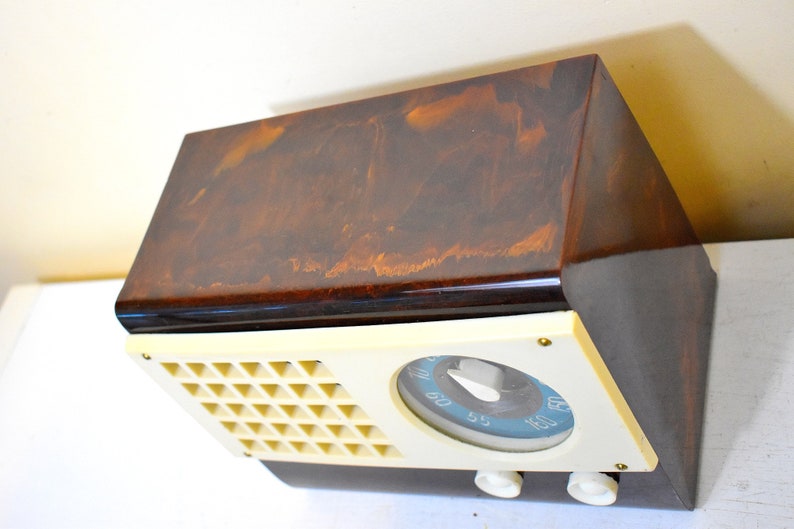 May include: A vintage brown and cream radio with a dial and three knobs. The radio has a marbled brown finish and a cream-colored front panel.