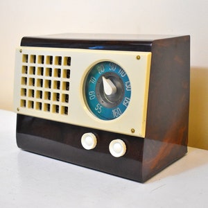 May include: A vintage brown and cream colored radio with a blue dial and a white knob. The radio has a speaker grille on the front and two knobs on the bottom.