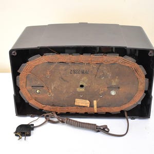 May include: A vintage black radio with a brown speaker and a power cord. The radio's back panel is visible, showing the speaker's components and a label with the text "7KW 228 2". The radio is on a white surface.
