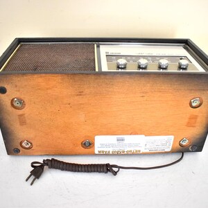 May include: A vintage wooden AM/FM radio with a black and silver face and a black cord. The radio has a label on the bottom that reads "Stereo Radio FM/AM".