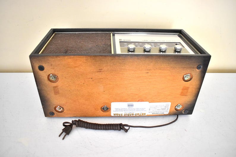 May include: A vintage wooden AM/FM radio with a black and silver face and a black cord. The radio has a label on the bottom that reads "Stereo Radio FM/AM".