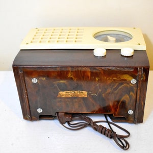 May include: A vintage brown and cream colored radio with a marbled plastic case. The radio has a dial with a needle and two knobs. The radio has a label on the back that reads "MULTI-FLEX 6-TUBE SUPER-HETERODYNE RADIO MADE IN U.S.A."