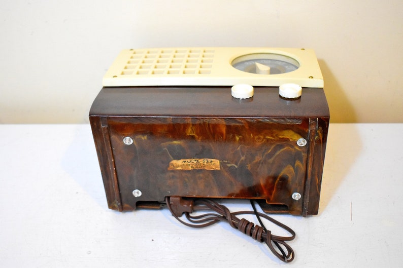May include: A vintage brown and cream colored radio with a marbled plastic case. The radio has a dial with a needle and two knobs. The radio has a label on the back that reads "MULTI-FLEX 6-TUBE SUPER-HETERODYNE RADIO MADE IN U.S.A."