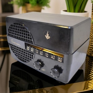 Puede incluir: Una radio Emerson vintage en gris y negro, con una rejilla de altavoz, dial de sintonizaci&oacute;n y visualizaci&oacute;n de frecuencia. La radio tiene un dise&ntilde;o retro con un logotipo en la parte superior. Una pieza cl&aacute;sica de decoraci&oacute;n del hogar.