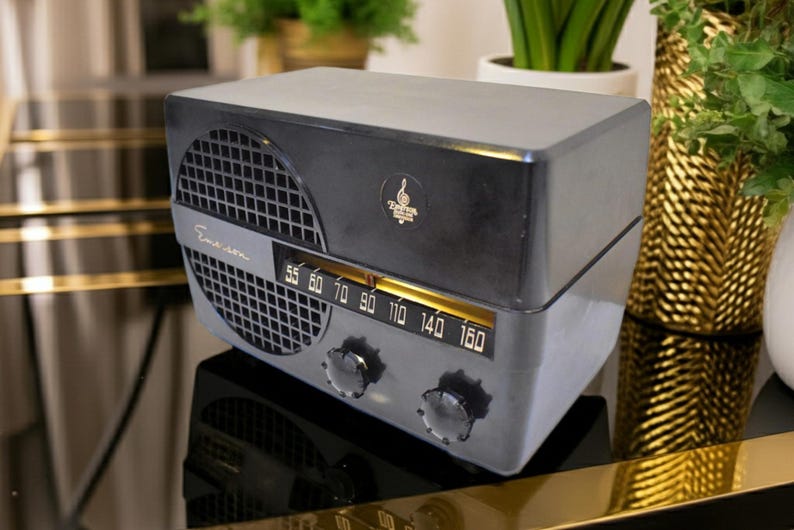 Puede incluir: Una radio Emerson vintage en gris y negro, con una rejilla de altavoz, dial de sintonizaci&oacute;n y visualizaci&oacute;n de frecuencia. La radio tiene un dise&ntilde;o retro con un logotipo en la parte superior. Una pieza cl&aacute;sica de decoraci&oacute;n del hogar.