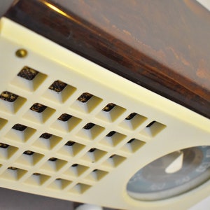 May include: A vintage radio with a brown wooden top and a white front panel. The front panel has a grid of small squares and a round dial with a needle.