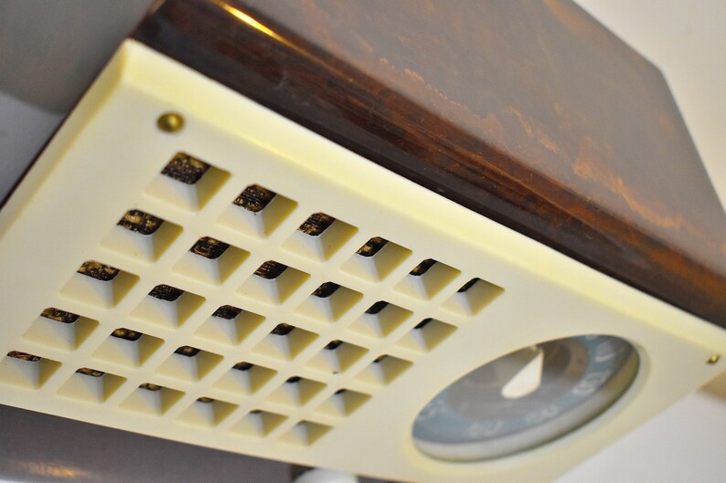 May include: A vintage radio with a brown wooden top and a white front panel. The front panel has a grid of small squares and a round dial with a needle.