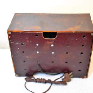 May include: The back of a vintage brown and red radio with a cord and plug. The radio has a brown plastic case and a red plastic back panel with multiple holes.