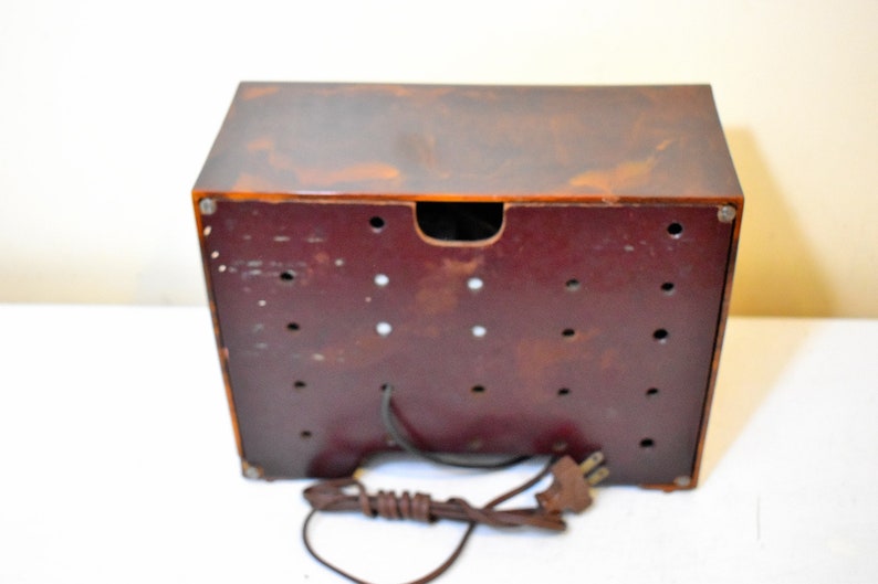 May include: The back of a vintage brown and red radio with a cord and plug. The radio has a brown plastic case and a red plastic back panel with multiple holes.