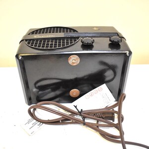 Puede incluir: Una radio Emerson negra vintage con una rejilla de altavoz, dos perillas y un cable de alimentaci&oacute;n. La radio tiene forma rectangular y un peque&ntilde;o emblema en la parte superior. Una etiqueta de papel est&aacute; adherida al cable de alimentaci&oacute;n.