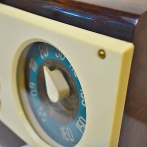 May include: Close-up of a vintage radio with a white face and a blue and white dial. The dial has numbers from 55 to 150. The radio has a brown wooden case.