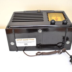 May include: A vintage black radio with a glossy finish. The radio has a speaker grill, two knobs, and a dial. The back of the radio has a label that reads "Retro Radio Park". A brown cord and plug are attached.