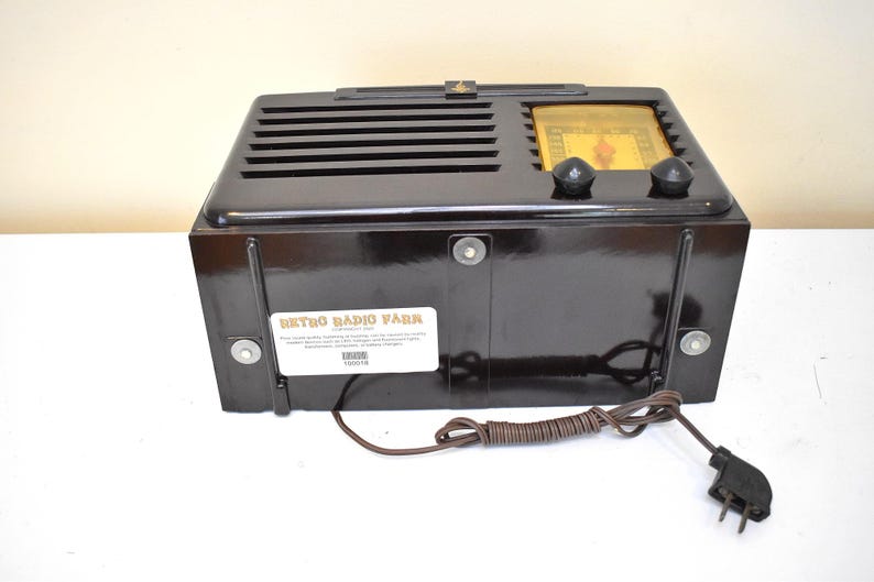 May include: A vintage black radio with a glossy finish. The radio has a speaker grill, two knobs, and a dial. The back of the radio has a label that reads "Retro Radio Park". A brown cord and plug are attached.