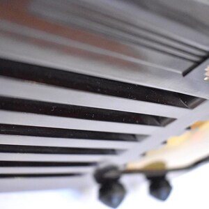 May include: Close-up of a black, vintage-style toaster. The toaster has a series of horizontal slots and a decorative emblem in gold. The image is taken from a low angle, highlighting the design and texture of the appliance.