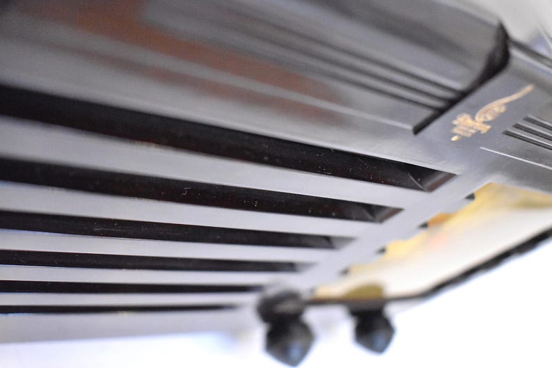 May include: Close-up of a black, vintage-style toaster. The toaster has a series of horizontal slots and a decorative emblem in gold. The image is taken from a low angle, highlighting the design and texture of the appliance.