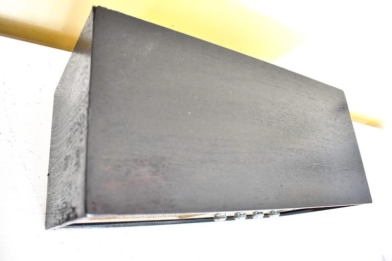 May include: A black wooden box with a textured surface. The box has a small, rectangular opening on the front with a row of silver knobs.