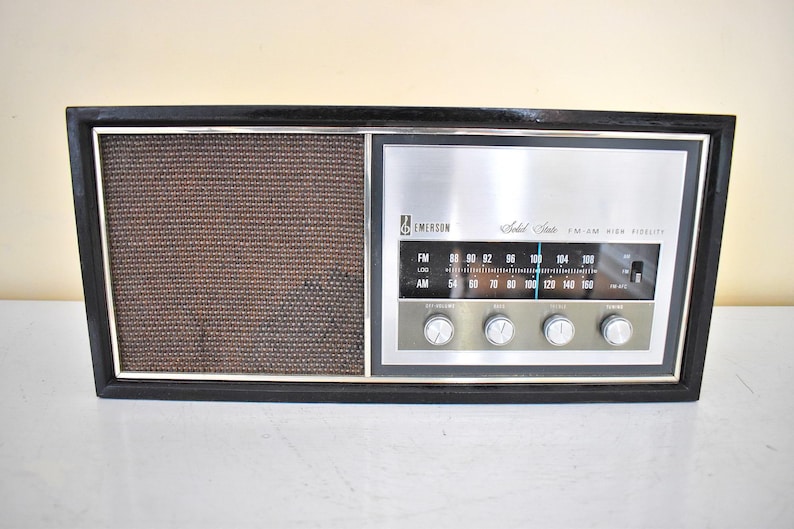May include: A black vintage Emerson Solid State AM FM High Fidelity radio with a silver face and a brown speaker grille.