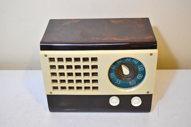 May include: A vintage, brown and cream colored radio with a blue dial and a knob for tuning. The radio has two white knobs on the front.