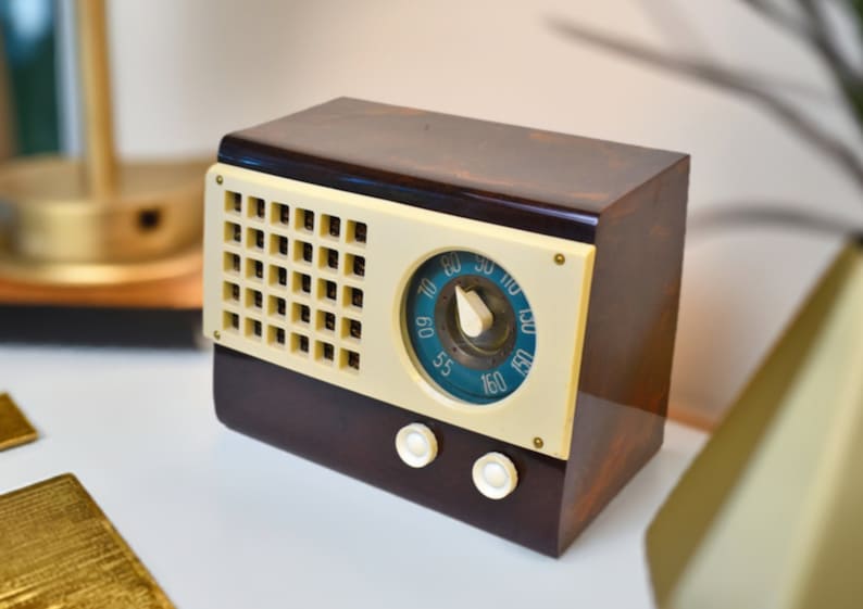 May include: A vintage brown and cream radio with a round dial and a grid of buttons. The dial has numbers from 55 to 160.